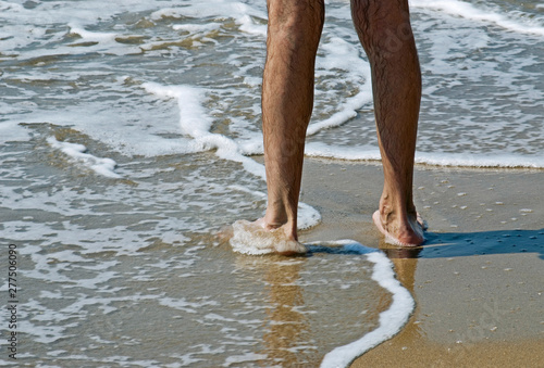 low section of a man standing barefoot on the wet sand