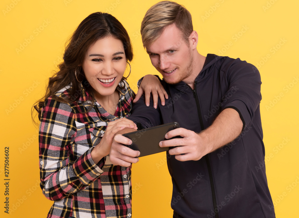 Enjoy man and woman while both using mobile phones play game over yellow background. Enjoy man and woman while both using mobile phones play game over yellow background.