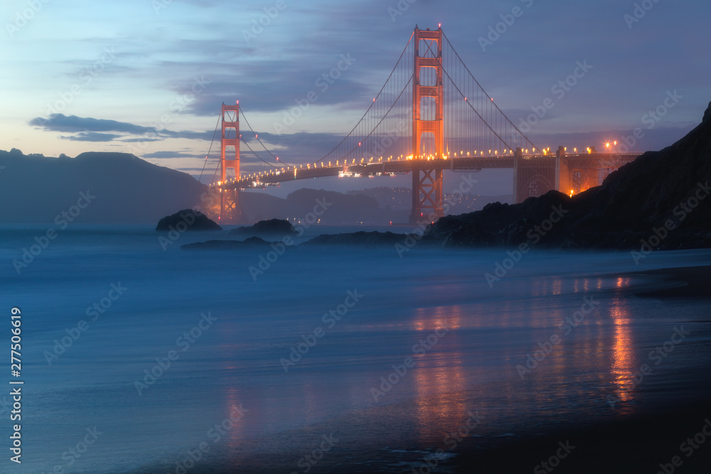 Fototapeta premium Classic panoramic view of famous Golden Gate Bridge seen from scenic Baker Beach in beautiful golden evening light on adusk with blue sky and clouds in summer, San Francisco, California, USA