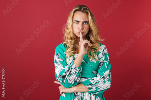 Displeased young pretty blonde cute woman in dress posing isolated over red wall background showing silence gesture.