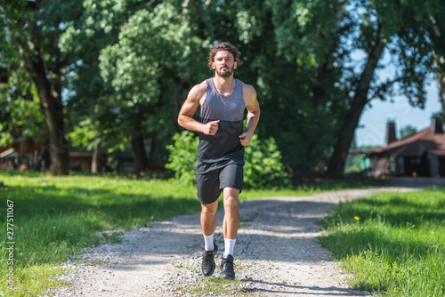 Young handsome man running on gravel road in nature 