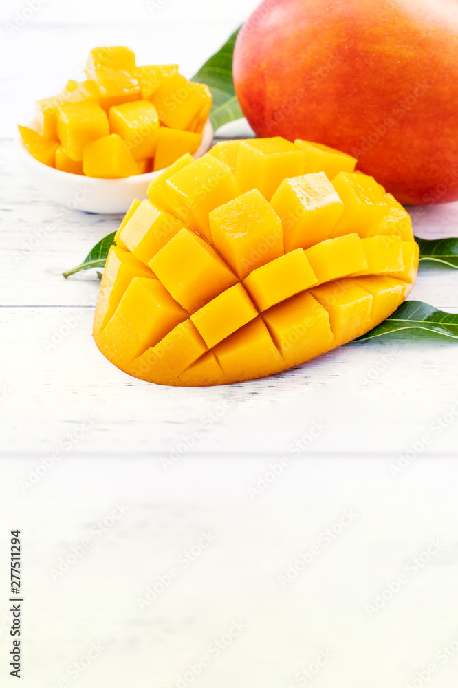 Beautiful chopped mango with green leaves on bright white color timber background. Above Top view, flat lay, copy space, close up. Tropical fruit concept.