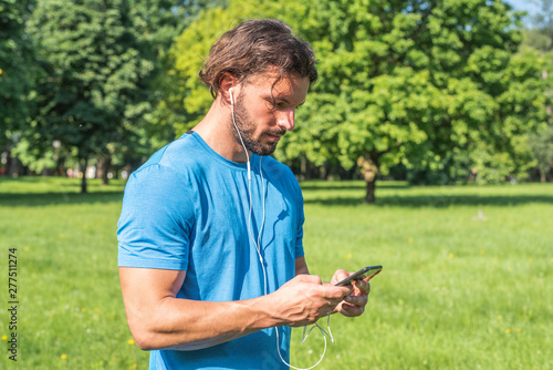Handsome man with beard listening to music in nature on smartphone
