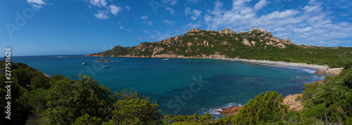 A wide panorama shot of a sandy beach and a blue ocean bay surrounded by green hills in bright sunlight.
