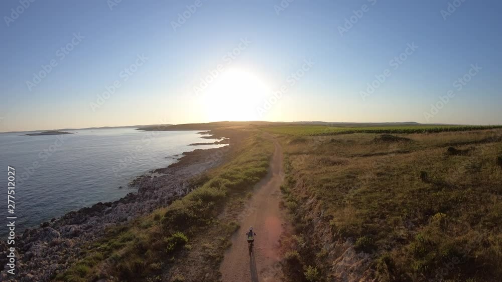 AERIAL  Mountain biker riding his bike on a trail along the sea at sunset