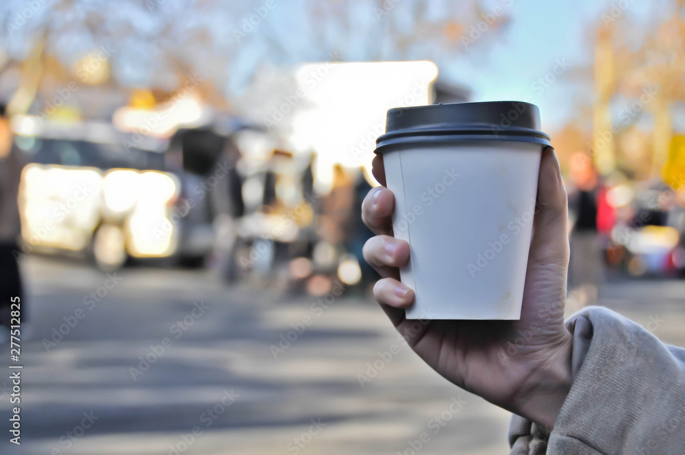 Take away white paper hot coffee cup with right hand holding in Sunday flea market Take away white paper hot coffee cup with right hand holding in Sunday flea market