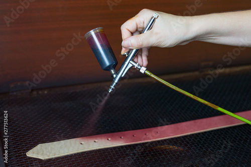 Leather craftsman causes paint on straps. Spray gun with purple paint. Handmade concept. Concept of small business to create leather products.