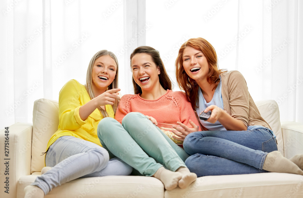 entertainment, leisure and friendship concept - three smiling teenage girls or friends with popcorn and remote watching tv at home