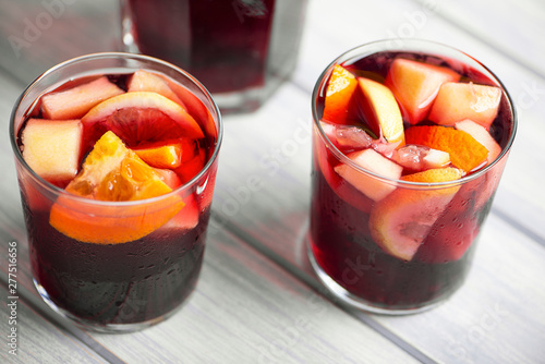 Two glasses next to a pitcher of sangria on wooden table. Typical Spanish drink made with wine and fruits.