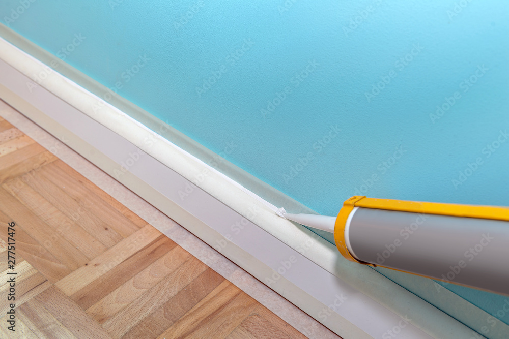 Foto de Mans hand caulk skirting board with caulking gun and silicone