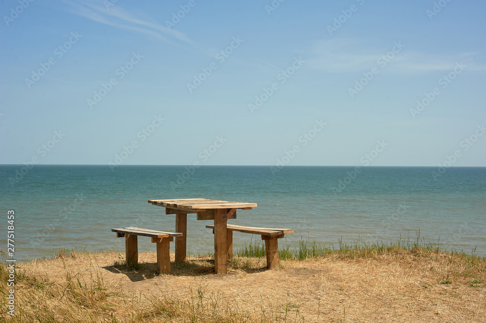 Table with benches on a cliff near the sea. Camping and wild recreation. Picnic in nature on the coast.