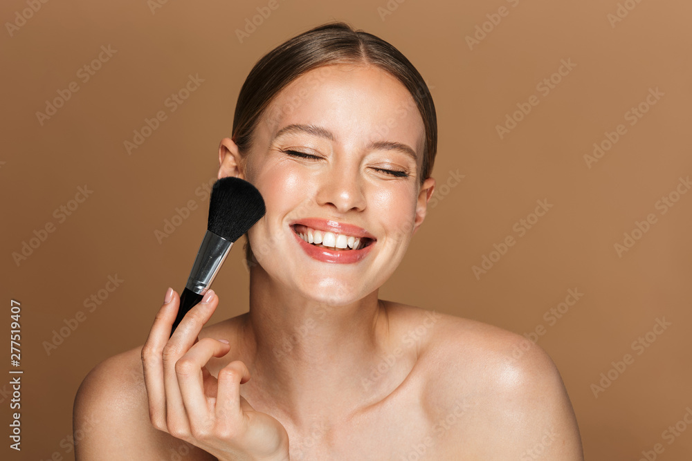 Image of joyful half-naked woman smiling at camera with closed eyes and using makeup brush Image of joyful half-naked woman smiling at camera with closed eyes and using makeup brush