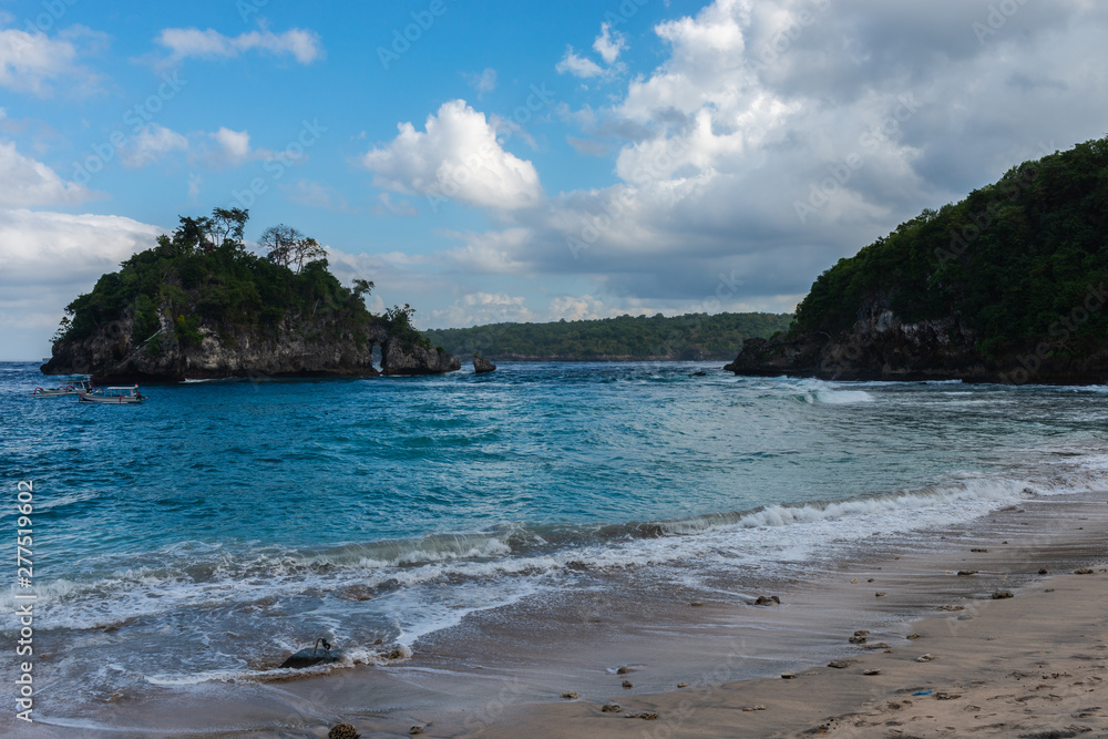 View of tropical beach, sea rocks and turquoise ocean, blue sky. Crystal Bay, Nusa Penida, Indonesia.