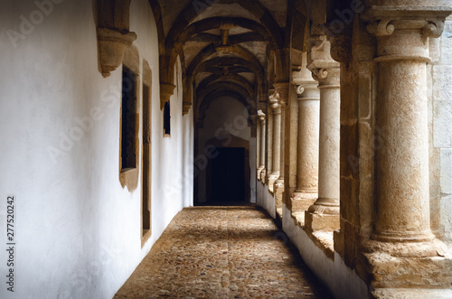Passagge through an antique medieval cloister with white wall and stone columns  leading to a distant door in an old portuguese monastery
