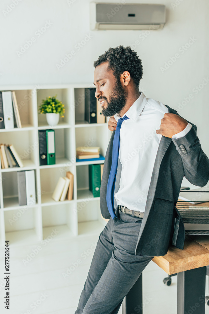 Fototapeta premium exhausted african american businessman undressing while suffering from heat in office