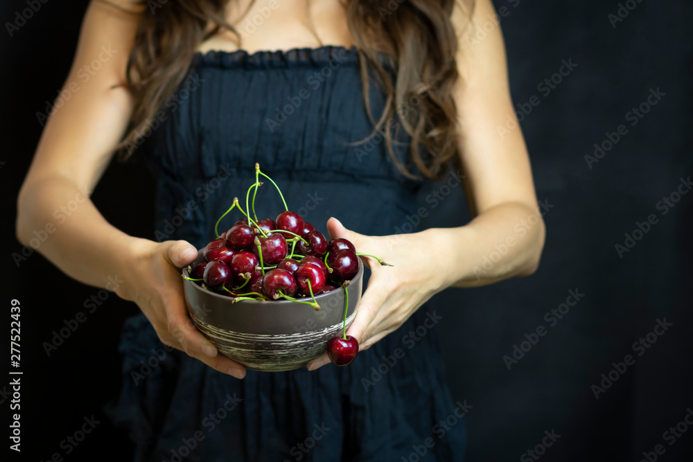Hands close-up on a dark background holding cherries. Open space, the concept of cinema, cosmetology. The concept of organic food and healthy lifestyle, healthy food, happiness and joy Hands close-up on a dark background holding cherries. Open space, the concept of cinema, cosmetology. The concept of organic food and healthy lifestyle, healthy food, happiness and joy