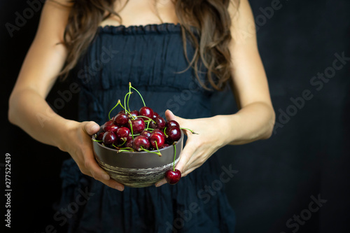 Hands close-up on a dark background holding cherries. Open space, the concept of cinema, cosmetology. The concept of organic food and healthy lifestyle, healthy food, happiness and joy