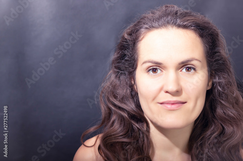 Happy, beautiful woman close up with dark hair on dark background. Open space, the concept of cinema, cosmetology. The concept of organic food and healthy lifestyle, healthy food, happiness and joy