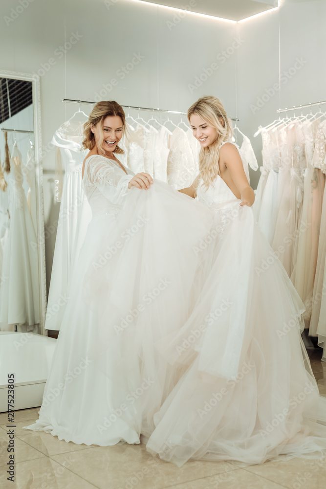 Two brides looking at the dresses of each other.