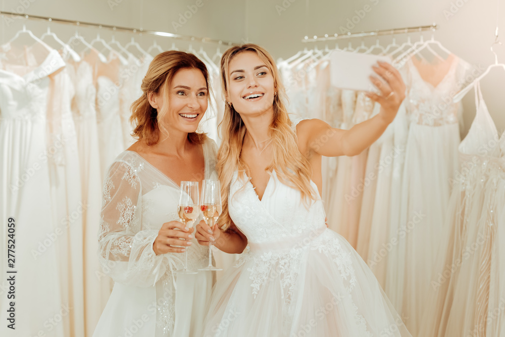 Two happy women taking selfies in wedding dresses.