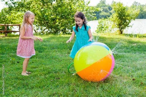 Kids play with water on hot summer day. Funny little girls freands playing with a water ball in the Sunny garden . Preschooler kids having fun with water spray. Summer outdoor activity for children photo