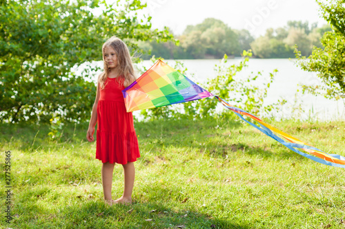 Child playing with a kite while running outdoors, sunset, in summer day. Funny time with family. Happy little girl launch a kite 