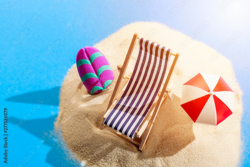 Miniature beach with deck chair, umbrella, parasol and surfboard on tropical islands sand surrounded by water. Tropical resort and vacation concept. Miniature beach with deck chair, umbrella, parasol and surfboard on tropical islands sand surrounded by water. Tropical resort and vacation concept.