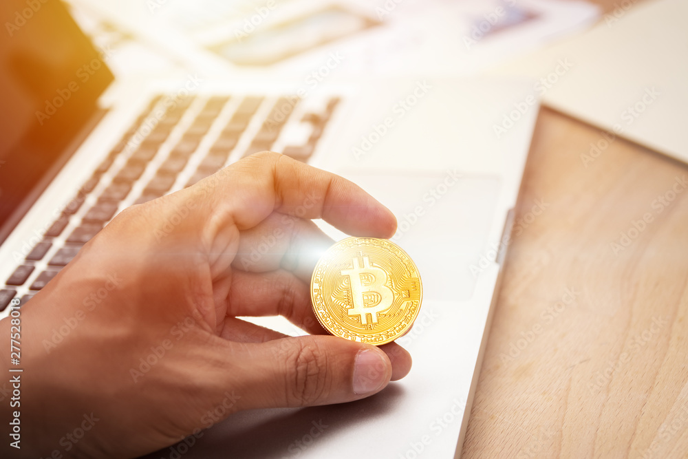 Fototapeta premium businessman holding cryptocurrency golden bitcoin coin in hand with computer laptop at background. crypto currency, electronic virtual money for web banking and international network payment
