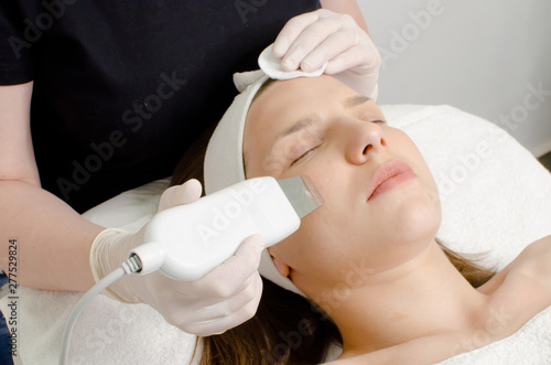 Cosmetologist,beautician in white gloves  making facial treatment with ultrasonic spatula to young woman,face skin scrubber treatment with ultrasonic spatula,facial cleansing procedure in beauty salon
