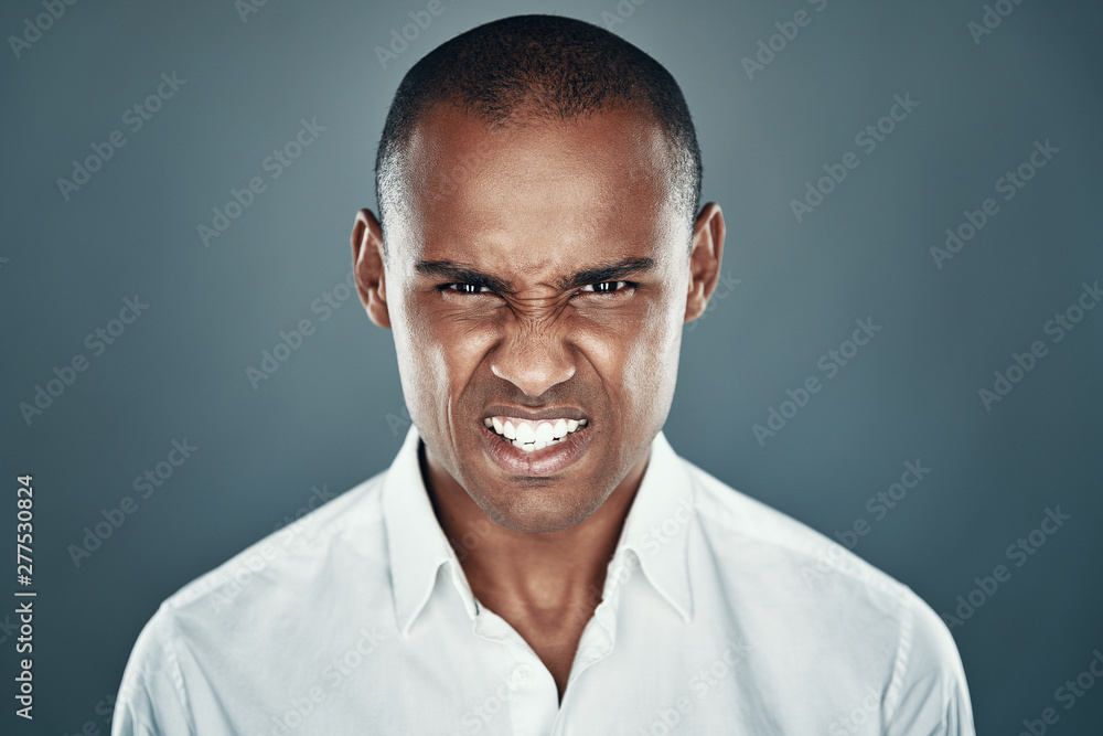Fototapeta premium Getting angry. Displeased young African man in shirt looking at camera and frowning while standing against grey background