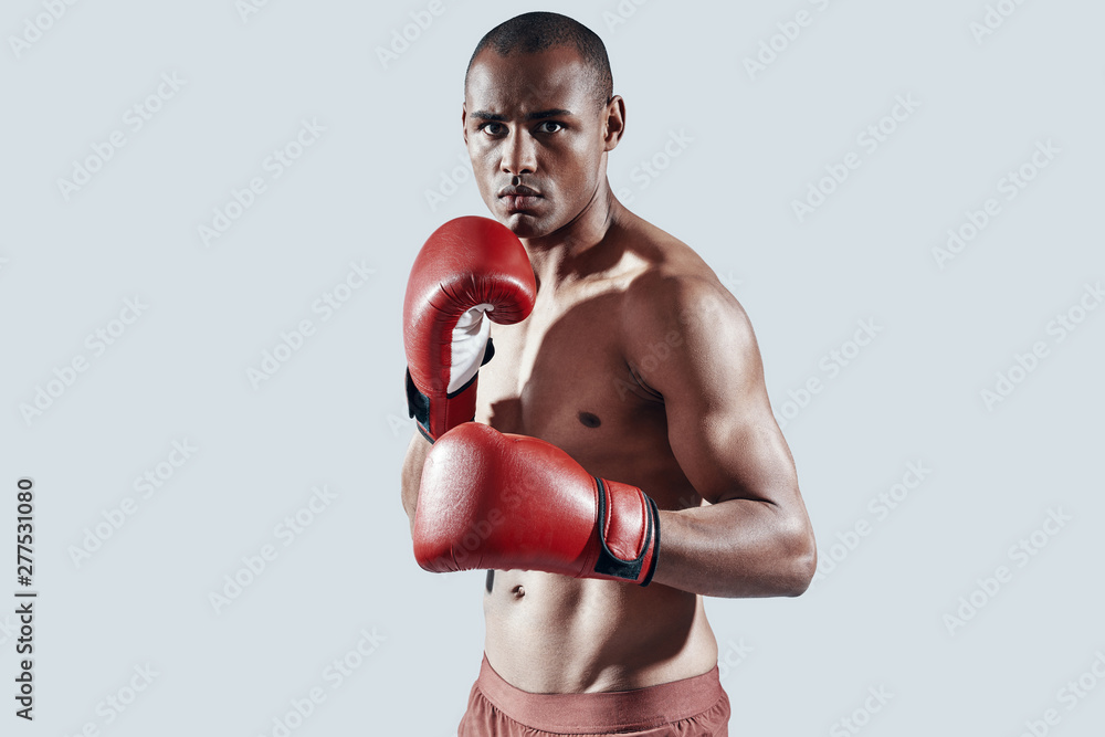 Confident boxer. Handsome young African man in red boxing gloves looking at camera while standing against grey background