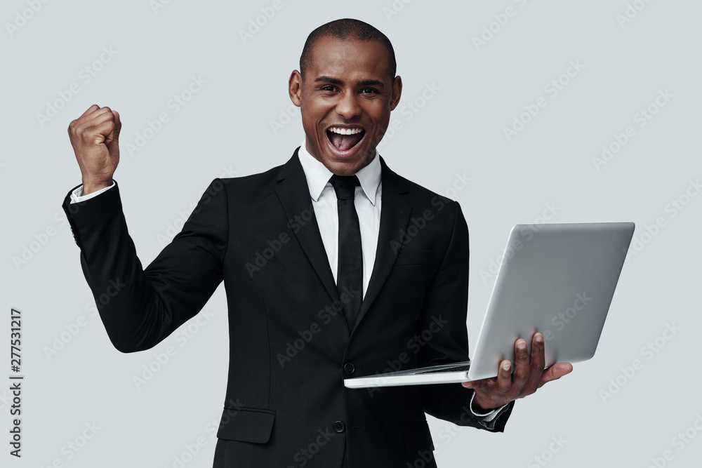 Success. Young African man in formalwear gesturing and smiling while standing against grey background Success. Young African man in formalwear gesturing and smiling while standing against grey background