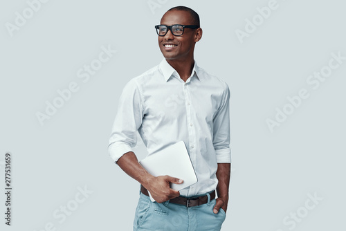 Smart and young. Handsome young African man using digital tablet and smiling while standing against grey background