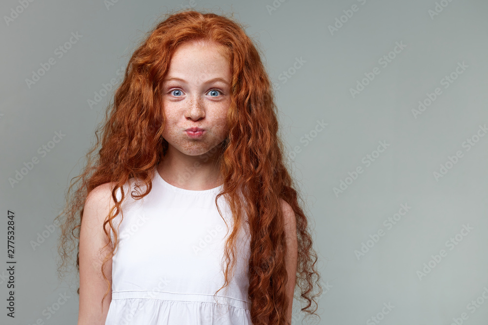 Cataract Hold op Centrum Portrait of funny little girl with ginger hair and freckles, surprised  looks at the camera, blows cheeks and looks funny, stands over gray  background. Stock Photo | Adobe Stock