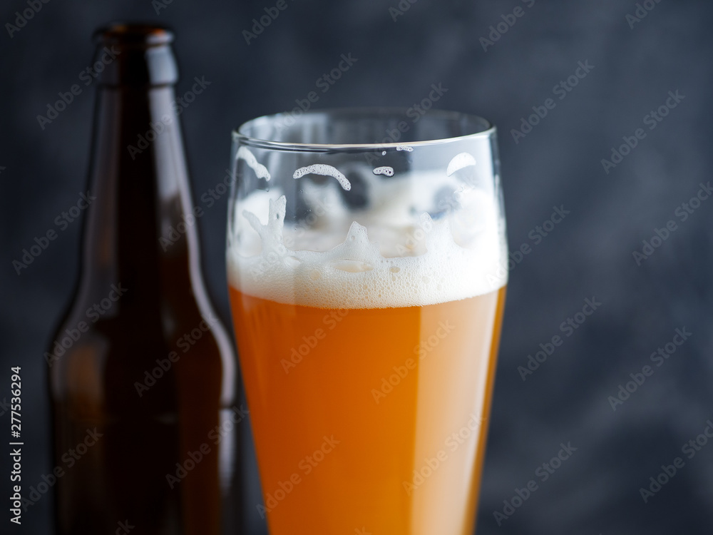 Close-up of a glass of cold unfiltered wheat beer and a beer bottle on a dark background