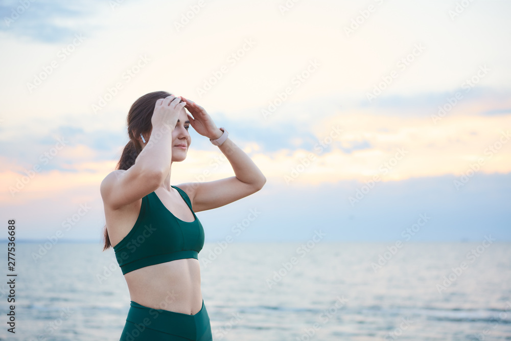 Young brunette woman exercising at the sea shore at sunrise listening to the music. Young brunette woman exercising at the sea shore at sunrise listening to the music.