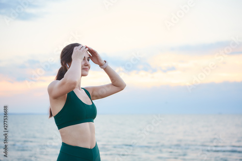 Young brunette woman exercising at the sea shore at sunrise listening to the music.