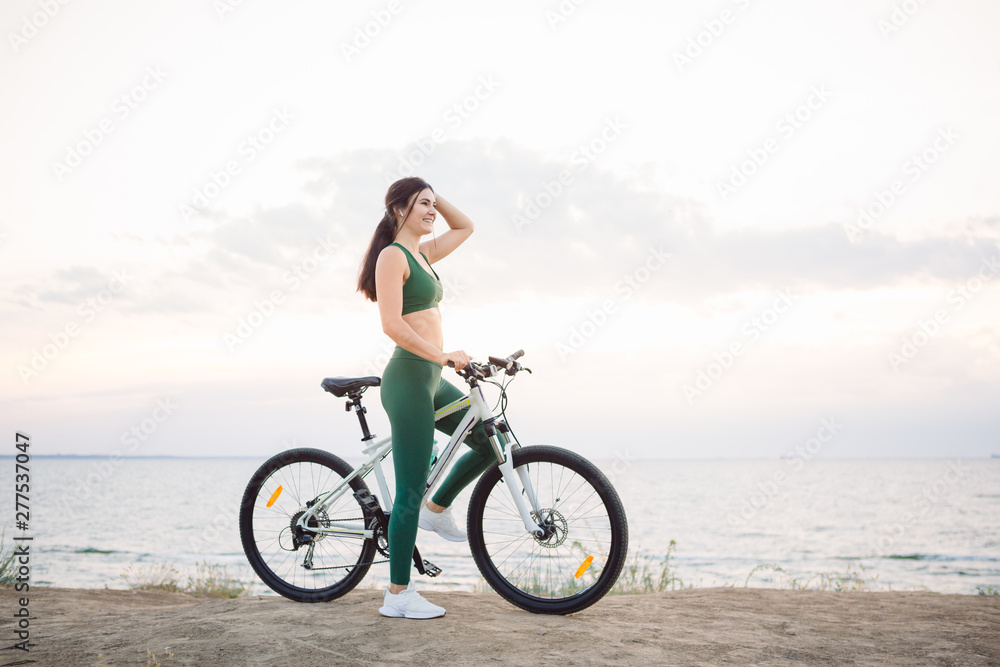 Fototapeta premium Young brunette woman on a bicycle at sunrise.
