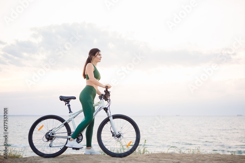 Young brunette woman on a bicycle at sunrise. © ianachyrva