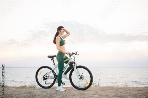 Young brunette woman on a bicycle at sunrise. © ianachyrva