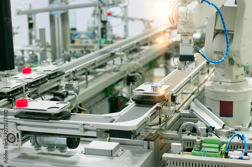 Focus on robotic arm's gripper. Industry 4.0 concept; artificial intelligence in smart factory. Robot picks up the product from automated car on the manufacturing line. Selective focus.