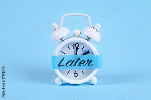 Procrastination, delay, urgency concept. White alarm clock with a sticky note with text later. photo