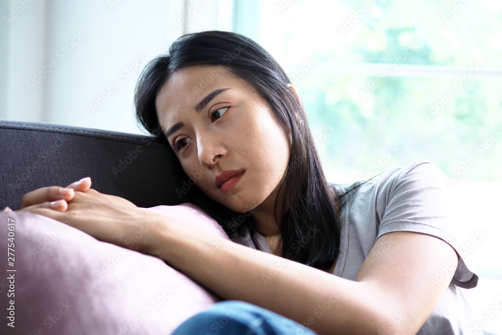 A beautiful Asian middle-aged woman has a sad and depressed expression on the couch in the house. A beautiful Asian middle-aged woman has a sad and depressed expression on the couch in the house.