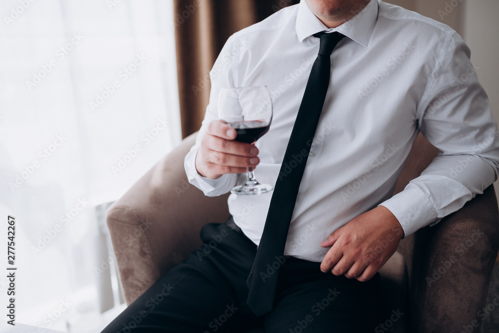 Foto Stock a man in a white shirt with a black tie and black trousers  holding a glass of red wine | Adobe Stock