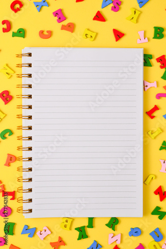 Open empty notebook and colorful letters on a yellow background. Top view. Space for text or design.