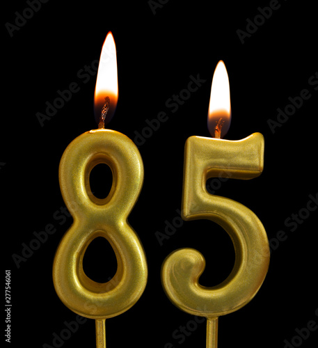 Burning golden birthday candles on black background, number 85