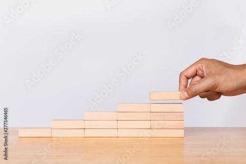 Bilde på lerret Hand arranging wooden cube stack a staircase on white background