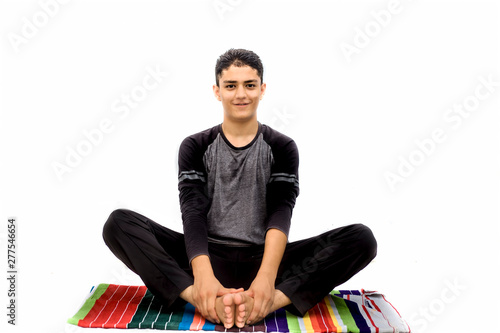 An energetic Young Caucasian teenager doing Bound Angle Pose or BAH-dah cone-AHS-anna pose practice isolated on white wearing black attire.