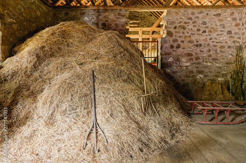 pile of hay with old fashioned pitchforks in an old stone barn lit by the sunlight coming in through the window at Hopewell Furnace National Historic Site in Pennsylvania