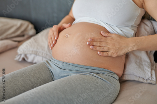 Young pregnant woman rubbing moisturising cream on her belly to moisturise her skin and reduce the possibility of stretch marks after childbirth photo